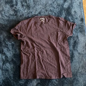 Brun t-shirt från Dobber med ficka - Snygg brun t-shirt från Dobber i storlek M. Modellen har rund hals, korta ärmar och en praktisk bröstficka. Tillverkad i mjuk bomull som känns skön mot huden. Perfekt för dig som gillar enkel och stilren design.