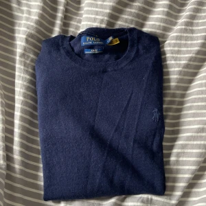 Marinblå merinoullströja Polo Ralph Lauren - Mörkblå, slim fit tröja från Polo Ralph Lauren i mjuk och tvättbar merinoull. Klassisk rund halsringning, långärmad och med diskret broderad logga på bröstet. Perfekt för dig som gillar stilrena och tidlösa plagg. Tröjan är knabbt använd och har inga defekter. Pris går att diskutera!