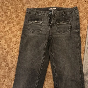 Grå bootcut jeans från Gina Tricot - Snygga grå jeans från Gina Tricot i storlek 164. Jeansen har bootcut-ben, klassiska fem fickor och cool tvättad look. Framfickor med extra detalj. Tillverkade i jeansmaterial med knapp och dragkedja framtill. Perfekta för dig som gillar en avslappnad men trendig stil.