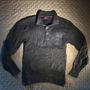 Mörkblå stickad tröja Tommy Hilfiger S/M - Mörkblå stickad tröja från Tommy Hilfiger med hög krage, tre knappar framtill och en bröstficka med lock. Tröjan har ribbade muddar och nederkant, perfekt för kyligare dagar. Klassisk och stilren design som funkar till det mesta. Använd 1/2 gånger och priset är inte fast så det är bara att komma med förslag. Skickar inom 24 timmar efter ni köpt