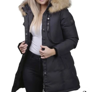 Svart dunjacka med äkta päls från Hollies - Snygg svart dunjacka från Hollies med stor huva kantad av brun päls. Jackan har flera fickor med lock och dragkedja, markerad justerbar midja och långa ärmar. Perfekt för kalla dagar med sin varma och fluffiga känsla. Klassisk och stilren design som funkar till allt. Jackan har legat i sin plastpåse därav mer ”platt päls”, går att skaka av till normal päls