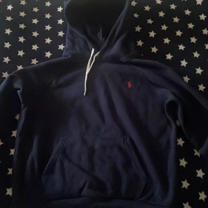 Mörkblå hoodie från Polo Ralph Lauren  - Mörkblå hoodie från Polo Ralph Lauren i storlek XL för kvinnor, M för man. Klassisk design med vit snörning i huvan, känguruficka och röd broderad logga på bröstet. Tillverkad i mjuk bomullsmix, perfekt för chill dagar. Priset är inte fast.