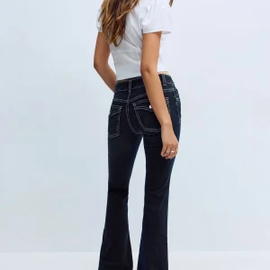 Mörkblå bootcut jeans från Gina - Snygga mörkblå jeans med bootcut passform och markerade vita kontrastsömmar. Klassisk femficksmodell med låg midja och utsvängda ben. Jeansen är tillverkade i ett stretchigt denimtyg som sitter bekvämt och framhäver siluetten.