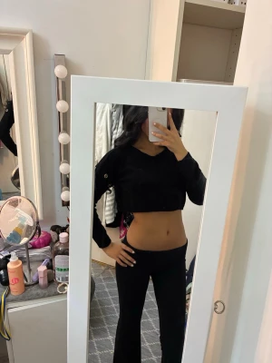 Svart croppad långärmad topp - Säljer en svart croppad långärmad topp i mjukt stickat material. Toppen har rund hals och coola metallringar som detalj på ärmarna. 