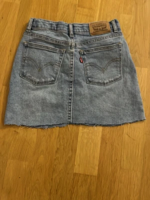 Levi's ljusblå jeanskjol - En ljusblå Levis jeanskjol med mönster på fickorna. Är stor i storleken och passar mig som har XXS/XS