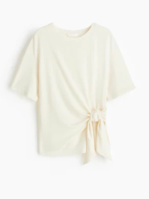  topp med knyt i sidan - Säljer en topp med rund hals och korta ärmar. Toppen har en snygg knytning i sidan som ger en cool och modern look. Materialet känns mjukt och lätt, perfekt för varmare dagar. Passformen är normal och toppen är enkel att matcha med både jeans och kjol.