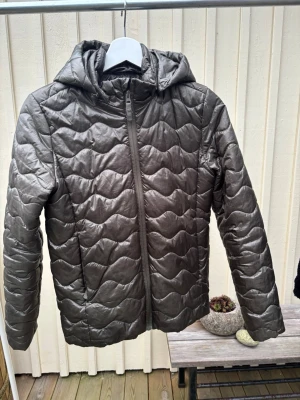 Mörkgrön quiltad pufferjacka - Säljer en mörkgrön jacka som är som small. Jackan har huva, dragkedja framtill och vågigt mönster i vadderingen. Skön att bära. Passar dig som gillar en enkel men snygg stil.