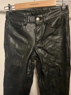 Svarta skinny byxor i skinnimitation - Säljer ett par svarta skinny byxor från Divided i storlek 34. Byxorna har fem fickor, bälteshällor och är gjorda i skinnimitation med snygg glansig finish. 