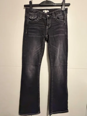 Svarta bootcut jeans från Gina Tricot - Svarta jeans från Gina Tricot i storlek 158 med kontrasterande vita sömmar och bootcut-ben. Jeansen har klassiska fickor fram och bak med lock och knappdetaljer. Materialet är jeans och passformen är normal.