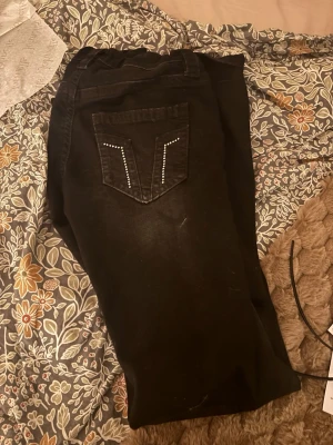 Svarta bootcut jeans från Gina Tricot - Snygga svarta jeans från Gina Tricot i bootcut-modell med hög midja. Jeansen har dekorativa nitar på bakfickan och klassisk knappstängning framtill. Perfekt för dig som gillar en stilren look med lite edge.