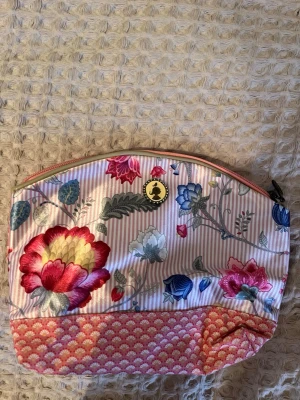 Blommig sminkväska/necessär från Pip Studio - Superfin sminkväska/necessär i tyg med blommigt mönster i rosa, rött, blått och vitt på ena sidan och rosa mönster på andra. Den har dragkedja och insidan är ljusrosa. Perfekt för att förvara sminkborstar, läppstift och andra sminkprodukter.