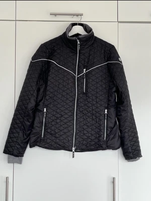 Svart ridjacka med dragkedjor -  Uhip Classic Diamond Jacket Jet Black, Storlek 44.  Ridjackan har en elegant design och med dess diamantformade quiltning har den en klassisk ridsportlook.  Jackan är tillverkad i ett lätt material med en figurnära passform och justerbar nederkant. Reflexpiping är över bröst, rygg och ärmar. Hög krage med ribbad insida samt stilrena ärmslut med invändiga muddar med hål för tummarna.  Nypris 1695kr, Säljes för 800kr 🖤