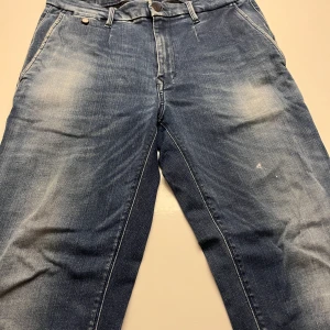 Replay Hyperflex blå jeans, storlek 31 - Snygga Replay Hyperflex jeans i blå tvätt med slitningar och klassisk femficksdesign. Jeansen har normal passform och är tillverkade i stretchigt jeansmaterial för extra komfort. Perfekt för dig som vill ha en cool och avslappnad look.
