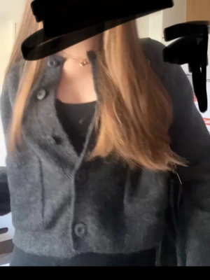 Mörkgrå kofta med knappar - Mysig mörkgrå kofta med stora knappar framtill. Koftan har en klassisk passform och är tillverkad i ett mjukt, stickat material som passar perfekt för kyligare dagar. Enkel att matcha med olika outfits och superbekväm att bära.