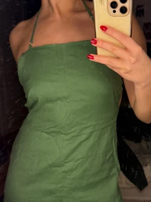 Grön ärmlös klänning med öppen rygg - Snygg grön klänning med raka linjer och smala axelband som korsas i ryggen. Klänningen är ärmlös och har en öppen rygg med minimalistisk design. Materialet känns lätt och svalt, perfekt för varma dagar. Passformen är normal och klänningen slutar nere vid anklarna. Är 163 centimer lång och den är perfekt för mig.