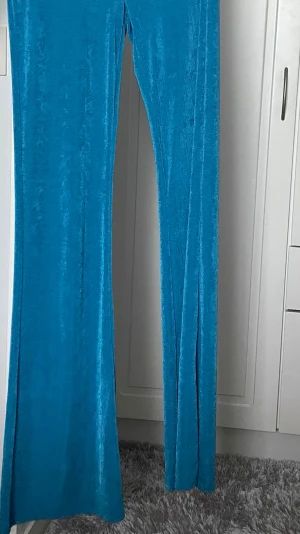 Blå vida byxor i sammet från Bershka - Säljer ett par blå, mjuka och glansiga byxor från Bershka i storlek S. Byxorna har en bred och rak passform med vida ben. Byxorna är helt oanvända (prislapp finns kvar) och köptes utomlands, men var tyvärr för stora för mig. 💙