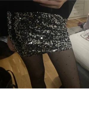 Svart paljettkjol  - Säljer en glittrig svart minikjol från New Yorker, täckt med silvriga paljetter som verkligen poppar. Kjolen är figurnära och har en kort passform som ger en snygg och festlig look. Helt ny med prislapp. 