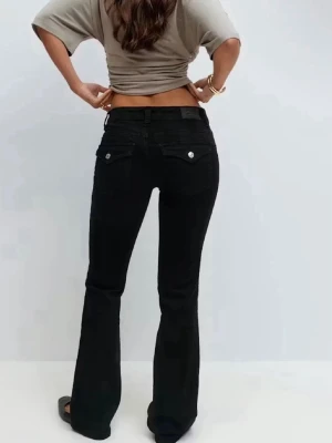 Svarta bootcut jeans - Snygga svarta jeans  med bootcut-snitt och klassiska fem fickor. Jeansen har låg midja och är tillverkade i ett mjukt och slitstarkt jeansmaterial. Perfekta för dig som gillar en tidlös och cool look.