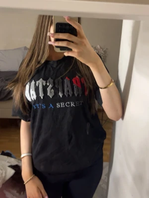 svart trapstar t shirt  - Säljer en svart t-shirt med coolt tryck i vitt, grått, rött och blått på framsidan. Texten har en edgy stil och t-shirten har en normal passform med korta ärmar. Perfekt för dig som gillar streetwear och vill sticka ut lite extra.