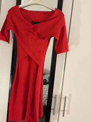 Röd omlottklänning från Amisu - Snygg röd klänning från Amisu med omlottdetalj framtill och korta ärmar. Klänningen har en feminin v-ringad hals och är tillverkad i ett mjukt material som ger en skön känsla.