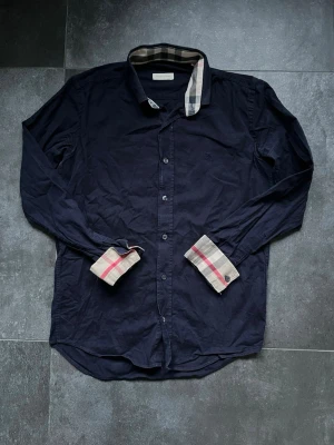 Burberry skjorta - Tjena, säljer nu denna riktigt snygga och populära burberry skjortan i bra skick, inga skavanker endast använd, storlek M, den är mörkblå men ser lite svart ut på bilderna, hör av er vid frågor och funderingar🙌🤝