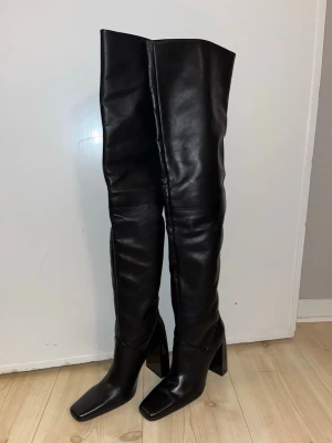 Nya läder stövlar  - Säljer ett par svarta overknee stövlar, som är tillverkade i slätt skinn. Snygg och stilren design som ger en cool vibe till outfiten. Nya med prislapp på.  