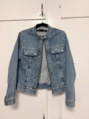 Blå jeansjacka från Lindex, strl 38 - Jeansjacka från Lindex som har används mycket. Lite missfärgningar men syns bara på nära håll. Saknar en knapp på ena armen. Annars bra