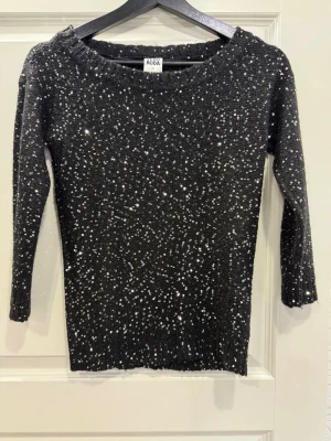 Svart paljettstickad tröja Vero Moda - Svart stickad tröja från Vero Moda med glittriga paljetter över hela ytan. Tröjan har rund halsringning.