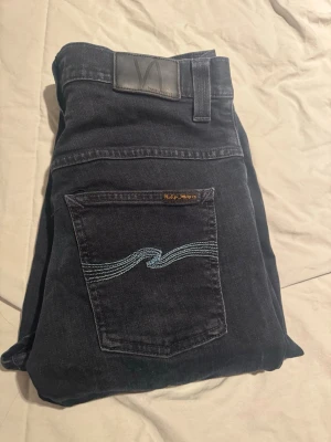 Mörkblå jeans från Nudie Jeans Co - Snygga mörkblå jeans från Nudie Jeans Co i klassisk femficksmodell. Jeansen har en cool broderad detalj på bakfickan och är tillverkade i slitstarkt bomullsmaterial. Passar dig som gillar stilrena och tidlösa jeans med schysst passform.