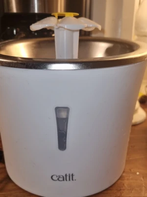 Ingen väst på bilderna - Bilderna visar ingen väst utan en vit och silverfärgad vattenfontän från Catit med en blomformad topp i plast. Ingen information om väst kan ges.