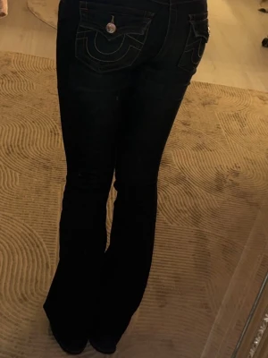 True Religion bootcut jeans mörkblå mid Rise - Säljer ett par mörkblå True Religion jeans, modell Becca Mid Rise Bootcut. Jeansen har snygga kontrastsömmar, ikoniska fickdetaljer bak och klassisk knappstängning. Materialet är jeans med en skön passform och bootcut-ben som ger en retrovibe. 