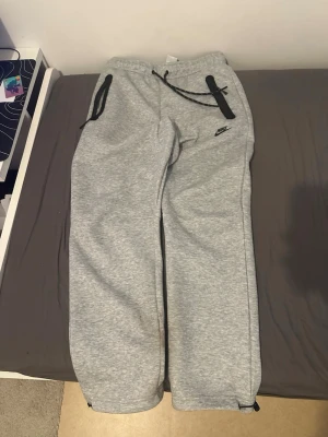 Nike tech open  - Säljer ett par grå mjukisbyxor från Nike med svarta detaljer. Byxorna har dragsko i midjan, svarta dragkedjor på fickorna och justerbar snörning vid bensluten. Tillverkade i mjukt bomullsmaterial för maximal komfort. Nike-logga broderad på ena benet.