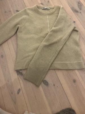Beige stickad tröja från Zara - Mysig beige stickad tröja från Zara med rund halsringning och ribbade muddar vid ärmslut och nederkant. Tröjan har en enkel, stilren design och är perfekt för lager på lager. Materialet känns mjukt och passar till många olika outfits.