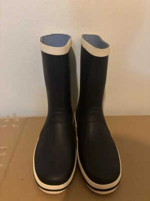 Gummistövlar  - Svarta stövlar från Sulman med vit kant upptill och vit sula knappast använt. Tillverkade i syntetmaterial som tål regn och blöta dagar. Perfekta för dig som vill ha stilrena och funktionella stövlar.
