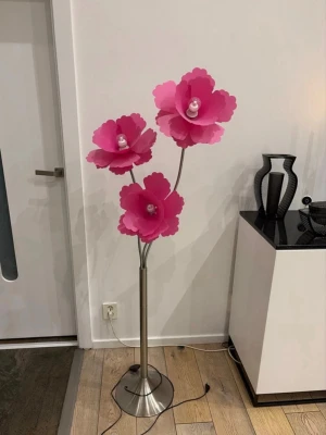 Golvlampa med rosa blomskärmar - Unik golvlampa med tre stora rosa blomformade lampskärmar. Lampan har en silverfärgad metallfot och ställning. Varje blomma har en glödlampa i mitten och ger ett coolt sken när den är tänd. Perfekt som statement piece i rummet.