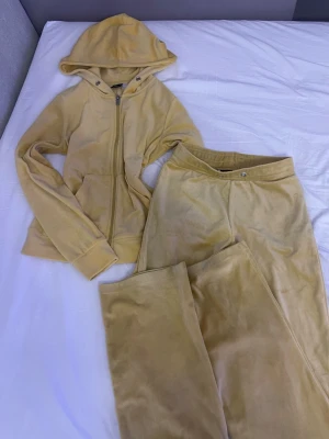 Beige velourset från Gina Tricot - Mysigt loungewear-set i beige velour från Gina Tricot. Setet består av en hoodie med dragkedja och fickor samt matchande byxor med resår i midjan. Perfekt för chill dagar hemma eller när du vill vara extra bekväm.