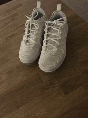 Vita Nike Air Vapormax sneakers - Säljer ett par helvita Nike Air Vapormax sneakers med genomskinlig sula och snygg snörning. Skorna har en futuristisk design med rund tå och detaljerade paneler på ovandelen. Perfekta för dig som vill ha en clean och modern look.