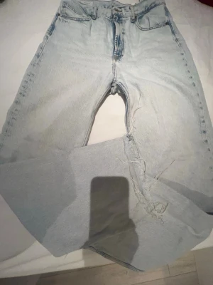 Ljusblå raka jeans - Ljusblå jeans med rak passform och klassisk femficksdesign. Jeansen har en hög midja och är tillverkade i denim av bomull. Slitna detaljer och trasor på ena benet ger en avslappnad och trendig look.