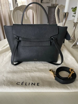 Céline Belt bag micro, svart skinn  - Snygg svart handväska från Céline i exklusivt skinn. Väskan har en stilren design med guldfärgade metalldetaljer, avtagbar axelrem och praktiskt ytterfack med dragkedja. Perfekt för dig som vill ha en klassisk och trendig accessoar. Väskan är i bra skick, små tecken på användning. Nypris ca 25 000 kr, säljer för 8500 kr. Äkthetsbevis & dustbag finns med. 