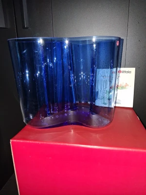 Blå Iittala Alvar Aalto vas - Säljer en ikonisk blå vas från Iittala, designad av Alvar Aalto. Vasen har en organisk, vågformad design och är tillverkad i glas. Perfekt som inredningsdetalj eller för blommor. Levereras med originalförpackning. Höjd: 16 cm, nyskick.