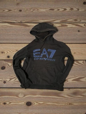 EA7 hoodie - En bekväm EA7 hoodie med bra passform frän M. Tröjan är skadad vid muddarna.Men annars ar det bra pris för en bekväm hoodie.