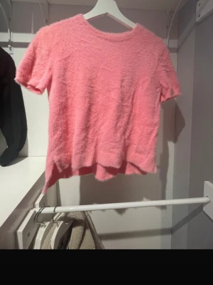 Ljusrosa fluffig topp från ASOS DESIGN - Supermjuk och fluffig ljusrosa topp från ASOS DESIGN. Kortärmad modell med rund hals och lätt loose fit. Perfekt för dig som vill ha en mysig men ändå stylish vibe. Materialet känns lent och har en lätt pälsig look.