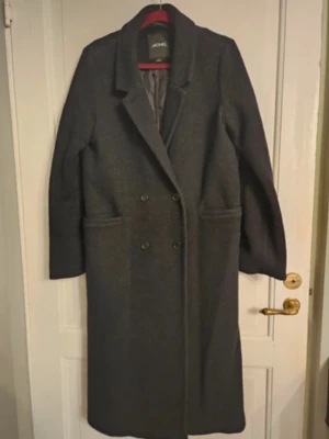 Svart kappa MONKI - Stilren svart kappa från MONKI med klassisk krage och dubbelknäppning framtill. Lång modell med raka ärmar och två stora fickor. Storlek S, säljer då jag fick en ny.