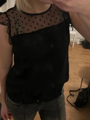 Svart blus - Snygg svart blus. Ärmlös modell med volangkant vid axlarna och rund halsringning. Perfekt för dig som vill ha en trendig och feminin topp.