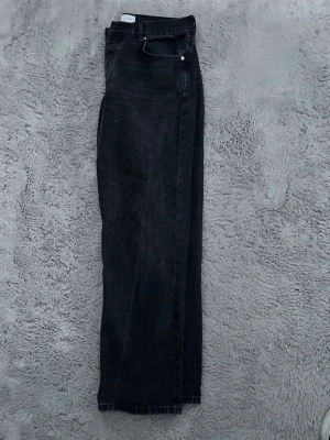 Svarta raka jeans från studio total  - Klassiska svarta studio total jeans med rak passform och femficksmodell. Jeansen har en tidlös look med knappgylf och subtila slitningar för en cool vibe. Perfekta till vardagsstilen och tillverkade i robust bomullsdenim.