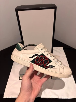 Gucci Ace  - Säljer ett par stilrena Gucci Ace sneakers i storlek 40. Skorna är använda men i ganska bra skick, med normalt slitage som syns på sulan och lätt på ovandelen (se bilder). Inget som påverkar användningen – fortfarande riktigt fräscha och snygga på foten.  Skorna kommer komplett med originalbox, dustbag och papper, vilket gör dem perfekta både för eget bruk eller som ett tryggt andrahandsköp.  📦 Originaltillbehör ingår 👟 Storlek: 40 