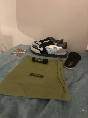 Valentino Garavani Rockrunner sneakers - Säljer ett par Valentino Garavani Rockrunner sneakers i svart, ljusblått och grått med coolt kamouflagemönster. Skorna har svarta snören, nitar på hälen och en platt sula. Materialmix av skinn och mocka. Kommer med extra skosnören och dustbag.