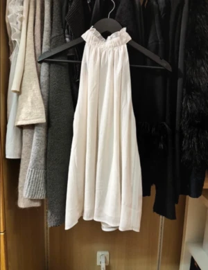 Vit ärmlös halterneck blus - Säljer en luftig vit blus med halterneck och volangkant vid halsen. Toppen är ärmlös och har en lätt A-linjeformad passning som ger ett flowy intryck. Perfekt till sommaren och enkel att styla med både jeans och kjol.