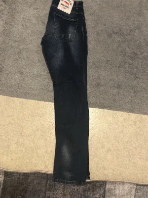 Mörkblå slim jeans Brothers - Säljer ett par mörkblå jeans från Brothers med snygg tvätt och slitningar på fickorna. Jeansen har fem fickor, normal midja och smal passform som sitter tajt längs benen. Klassisk jeanslook med dragkedja och knapp framtill.