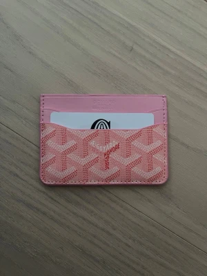 Rosa korthållare  - Säljer en snygg rosa korthållare från med deras ikoniska mönster. Plånboken har flera fack för kort och är tillverkad i skinn med ett stilrent och lyxigt utseende. Perfekt för dig som vill ha något både praktiskt och trendigt.